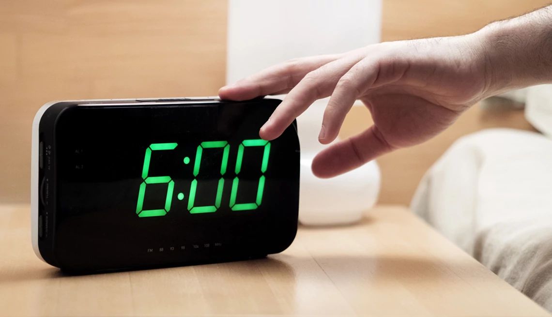 a hand reaching for an LED digital alarm clock that reads six a.m.